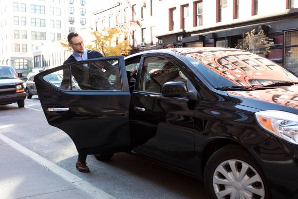 Young man, businessman getting into the back of a black car on a beautiful sunny day, door is open as he gets into the car with his briefcase, Commuting to work or going to the airport - limo service peoria, il